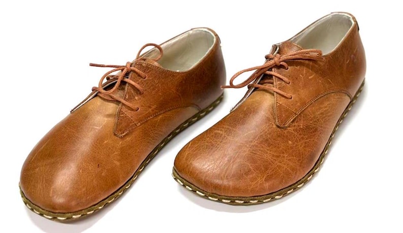 May include: A pair of brown leather lace-up shoes with a stitched sole.