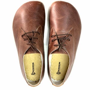 May include: A pair of brown leather lace-up shoes with a white insole. The insole has the text "Kramer Handmade in Italy" printed on it.
