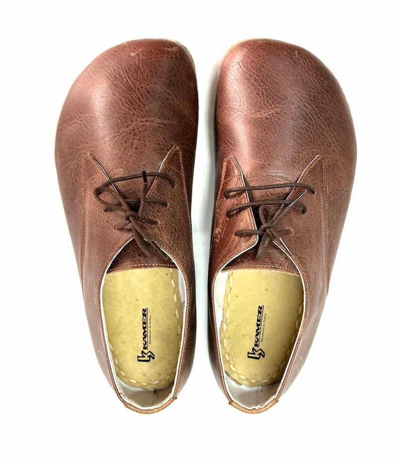 May include: A pair of brown leather lace-up shoes with a white insole. The insole has the text "Kramer Handmade in Italy" printed on it.
