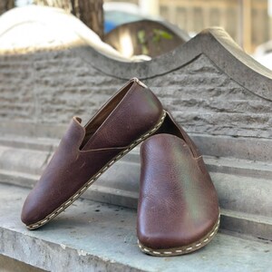 K&ouml;nnte beinhalten: Ein Paar braune Slipper aus Leder mit wei&szlig;en N&auml;hten an der Sohle.