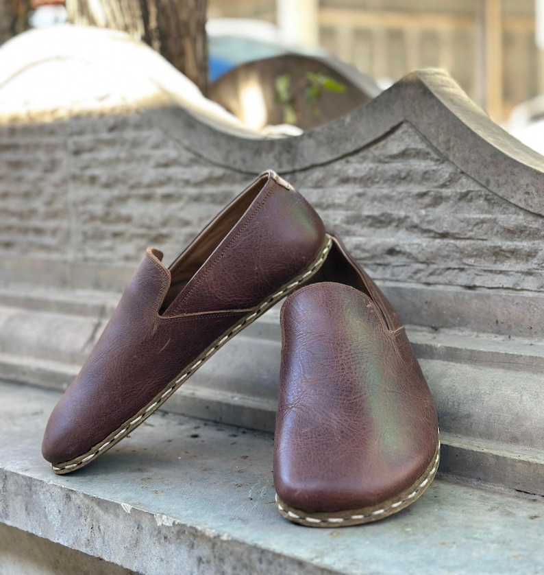 K&ouml;nnte beinhalten: Ein Paar braune Slipper aus Leder mit wei&szlig;en N&auml;hten an der Sohle.