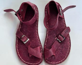 Puede incluir: Un par de sandalias de cuero burdeos con correas de tobillo ajustables y hebillas. Las sandalias tienen un diseño simple y minimalista y están hechas de cuero de alta calidad.
