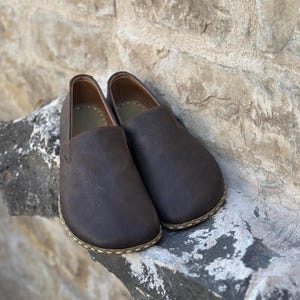 May include: A pair of brown leather slip-on shoes with a stitched edge.