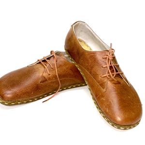 May include: A pair of brown leather lace-up shoes with a stitched edge. The shoes have a rounded toe and a low heel.