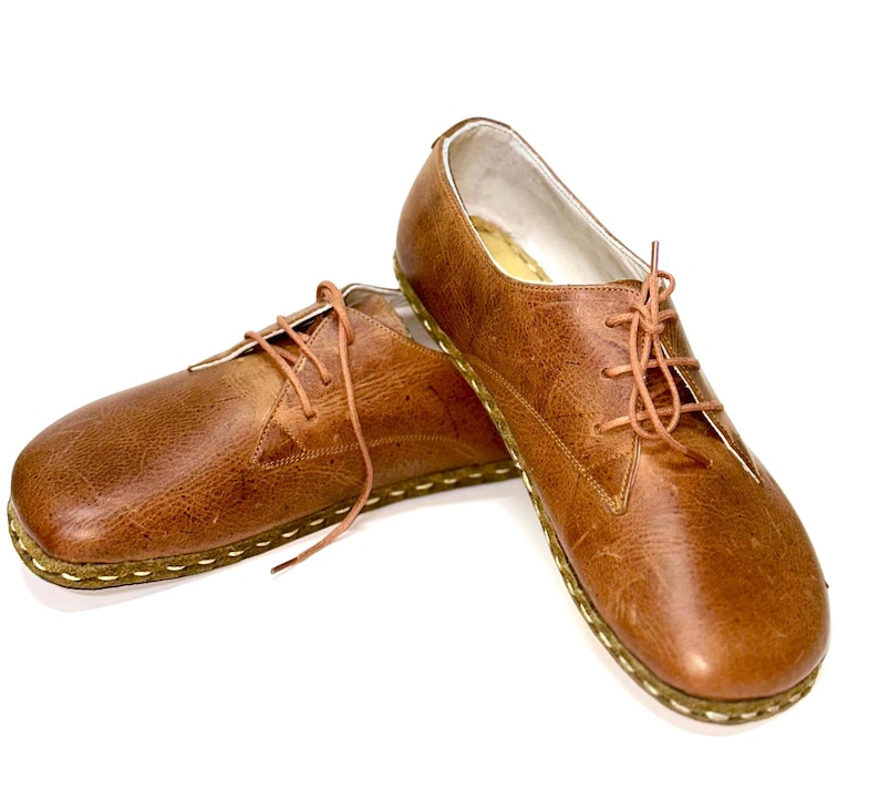 May include: A pair of brown leather lace-up shoes with a stitched edge. The shoes have a rounded toe and a low heel.