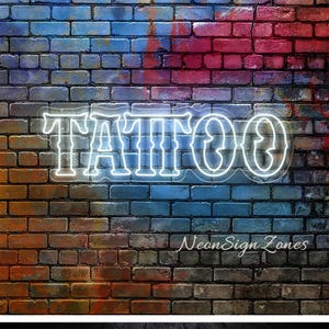 May include: A neon sign with the word "TATTOO" in white, outlined letters. The sign is mounted on a brick wall with a gradient of colors, including blue, red, and brown. The text "Neon Sign Zones" is below the word "TATTOO".