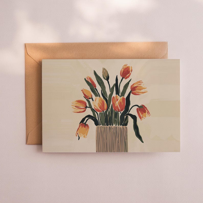 May include: A greeting card featuring a watercolor painting of orange and yellow tulips in a striped vase. The card is paired with a brown envelope, set against a cream-colored background. The floral artwork evokes a sense of spring.