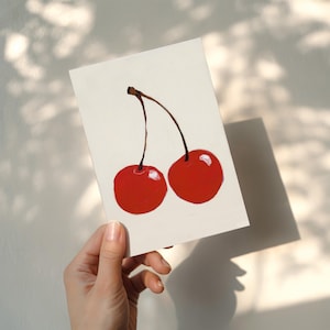 Puede incluir: Una obra de arte pintada a mano con dos cerezas rojas brillantes con tallos marrones sobre un fondo blanco. Las cerezas tienen un acabado brillante. La imagen est&aacute; iluminada por luz natural, proyectando una sombra.