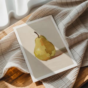 May include: A print featuring a still life of a pear. The pear is painted in shades of yellow and green, with a brown stem. The artwork is on a white background, resting on a wooden surface with a checkered cloth.