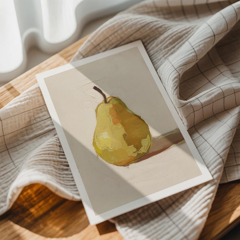 May include: A print featuring a still life of a pear. The pear is painted in shades of yellow and green, with a brown stem. The artwork is on a white background, resting on a wooden surface with a checkered cloth.