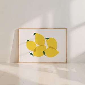 May include: A framed art print featuring a minimalist design of overlapping yellow lemons with green leaves on a white background. The artwork is set in a light brown wooden frame, suitable for kitchen or dining room decor.