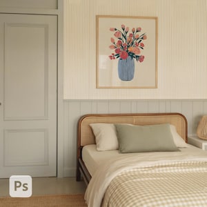 May include: A bedroom scene featuring a framed floral print above a bed with a rattan headboard. The artwork showcases a blue vase filled with pink and orange flowers. The bed has white and green pillows and a beige and white checkered blanket.