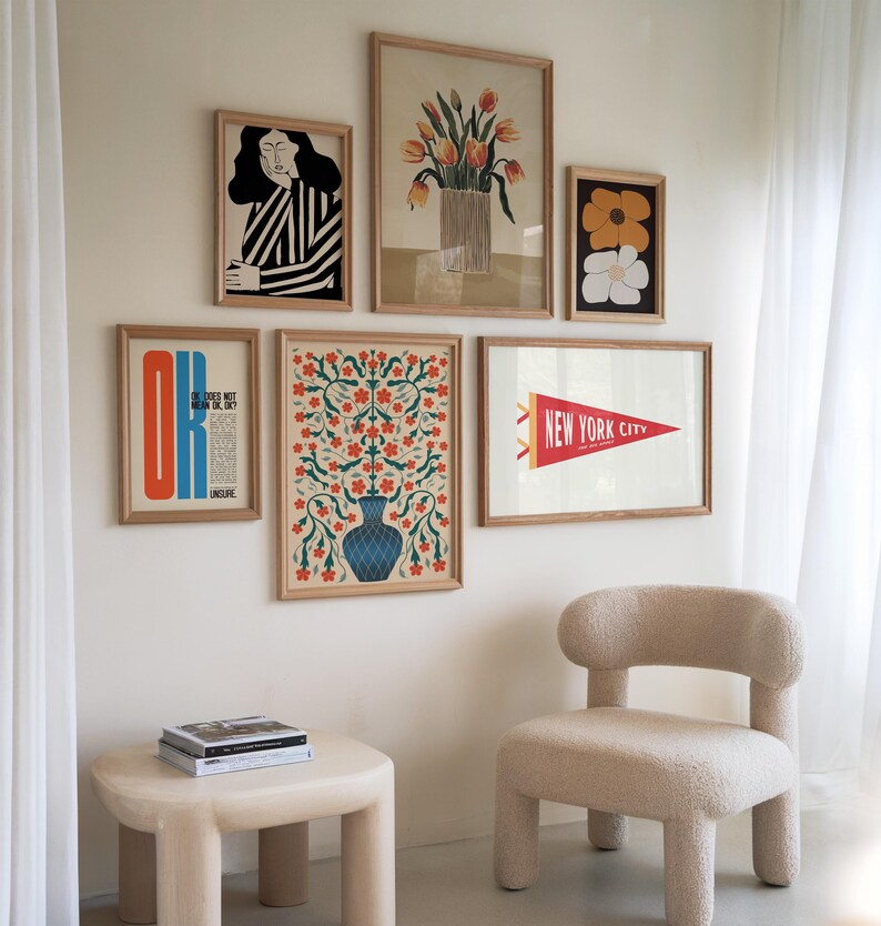 May include: A wall gallery featuring six framed prints. The prints include a floral design, a woman's portrait, a flower design, a New York City pennant, and a text-based print. The prints are arranged in a symmetrical pattern on a white wall.