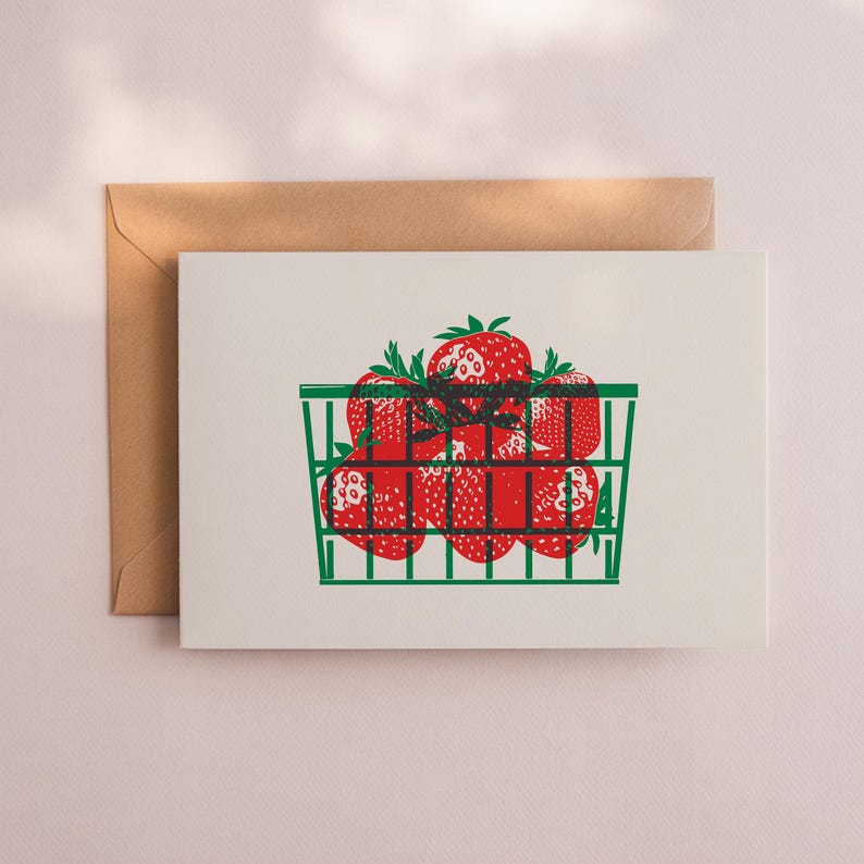 May include: Greeting card featuring a green basket filled with red strawberries. The strawberries have green stems and are printed on a white background. A brown envelope is behind the card.