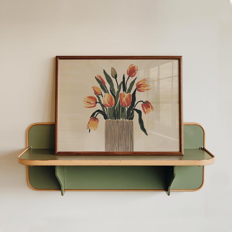 K&ouml;nnte beinhalten: Ein gerahmter Druck eines Strau&szlig;es aus orangefarbenen und gelben Tulpen in einer gestreiften Vase. Der Druck wird auf einem gr&uuml;nen Regal mit einer hellbraunen Verkleidung gezeigt.