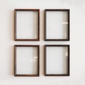 Könnte beinhalten: Vier braune Holzrahmen mit Glasscheiben sind in einem quadratischen Muster an einer weißen Wand angeordnet.