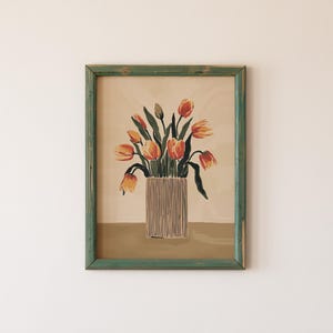 May include: A framed print of a still life featuring a bouquet of orange and red tulips in a striped vase. The background is a light beige color.