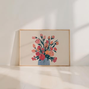 May include: A framed art print featuring a floral arrangement in a blue vase. The flowers are in shades of pink, red, and orange, with green stems and leaves. The background is a light beige color, and the frame is a natural wood tone.