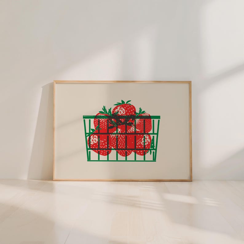 May include: A framed print featuring a green basket filled with red strawberries. The strawberries have green stems and are arranged in a grid-like pattern. The print is set against a cream-colored background and framed in a light wood.