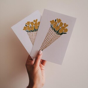 K&ouml;nnte beinhalten: Zwei wei&szlig;e Karten mit einer handgezeichneten Illustration eines Strau&szlig;es gelber Blumen in einem braunen und wei&szlig;en Korb. Die Blumen sind kegelf&ouml;rmig angeordnet und haben gr&uuml;ne Stiele.