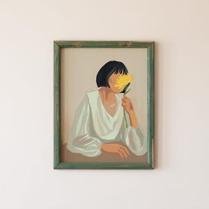 May include: A framed illustration of a person with short dark hair holding a yellow flower in front of their face. The person is wearing a white shirt and is sitting at a table.