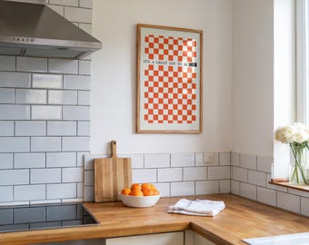 Puede incluir: Una impresión enmarcada con un patrón de cuadros rojos y blancos y el texto "Es un gran día para ser feliz". La impresión está colgada en una pared de azulejos blancos en una cocina.
