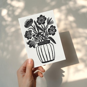 Puede incluir: Impresi&oacute;n art&iacute;stica en blanco y negro que representa un jarr&oacute;n con flores estilizadas. El jarr&oacute;n tiene rayas verticales. La impresi&oacute;n se sostiene en una mano, con sombras en el fondo.