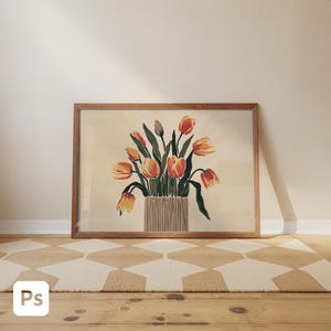 May include: A framed art print featuring a watercolor illustration of orange and yellow tulips in a striped vase. The artwork is set against a cream background and framed in a light brown wooden frame. The print is displayed on a wooden floor, with a geometric patterned rug in front.
