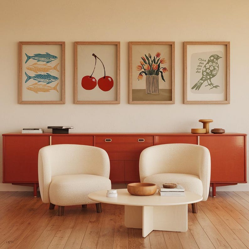 May include: A living room interior with a red cabinet, two white armchairs, and a coffee table. The wall above the cabinet is decorated with five framed prints, including a print of cherries, a print of fish, a print of flowers, and a print of a bird.