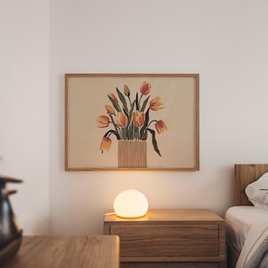 May include: A framed print of a watercolor painting of a bouquet of orange and yellow tulips in a vase. The print is hanging on a white wall above a wooden nightstand with a white globe lamp.