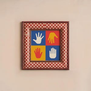 May include: A framed print with a red, white, and blue checkered border. The print features four colorful handprints in a grid pattern.