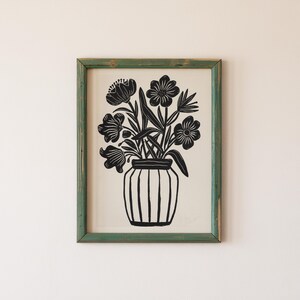 May include: Black and white print of a vase with flowers. The vase is a simple, cylindrical shape with vertical lines. The flowers are stylized and have a simple, geometric design.