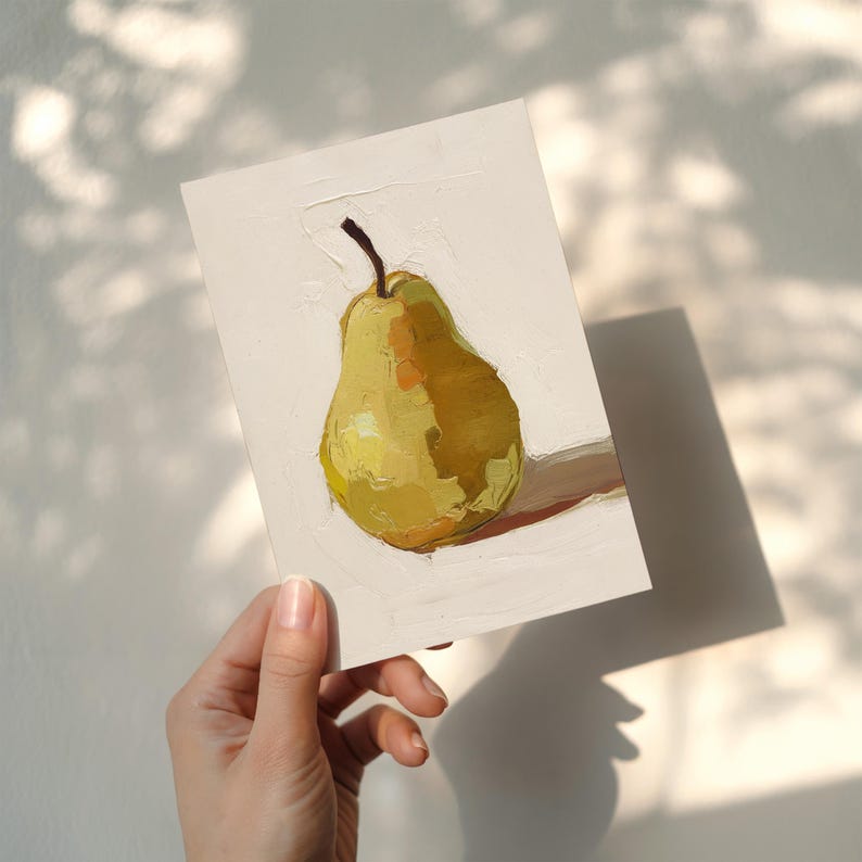 Puede incluir: Pintura al &oacute;leo de una pera amarilla con un tallo marr&oacute;n sobre un fondo blanco. La pera est&aacute; pintada con pinceladas visibles, y la obra de arte est&aacute; sostenida por una mano. La pintura est&aacute; iluminada por la luz del sol, proyectando una sombra.