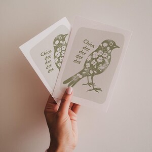 K&ouml;nnte beinhalten: Zwei gr&uuml;ne und wei&szlig;e Gru&szlig;karten mit einer Vogel-Illustration und dem Text "Chica dee dee dee dee" auf jeder Karte.