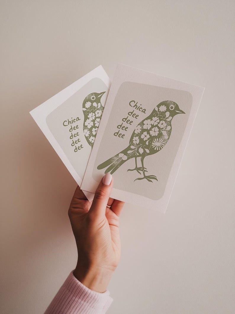 K&ouml;nnte beinhalten: Zwei gr&uuml;ne und wei&szlig;e Gru&szlig;karten mit einer Vogel-Illustration und dem Text "Chica dee dee dee dee" auf jeder Karte.
