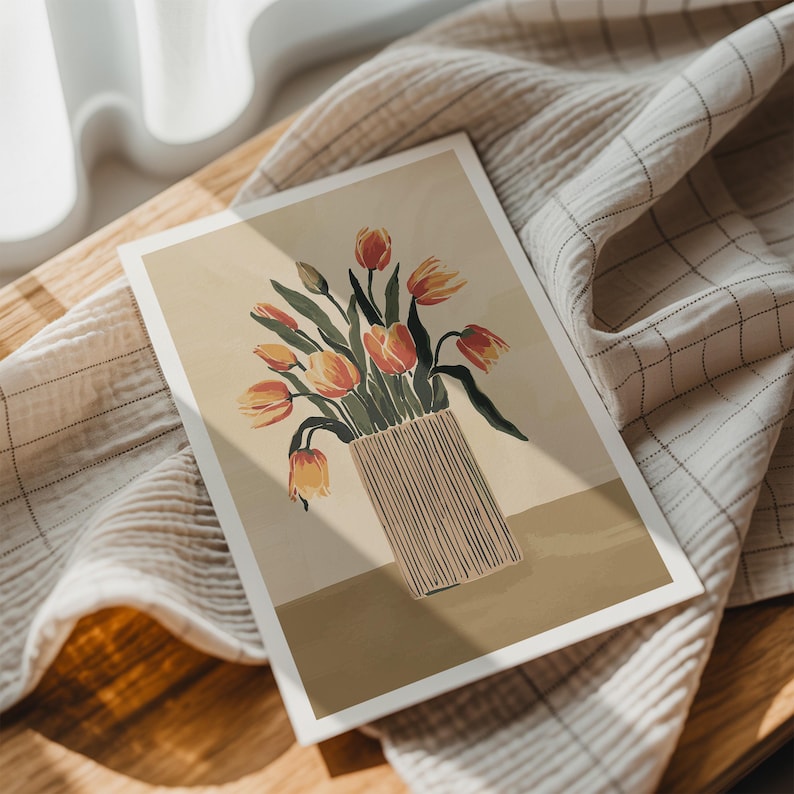 May include: A floral art print featuring a vase of orange and yellow tulips. The vase is beige with vertical lines. The print is on a white-bordered rectangular card, resting on a beige and white checkered cloth.