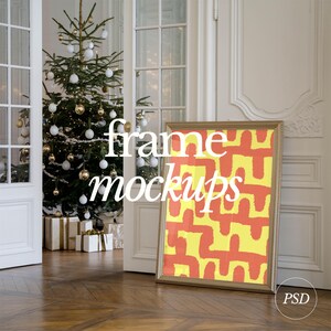 May include: A gold frame mockup with a yellow and orange abstract design inside. The frame is leaning against a white wall in a room with a Christmas tree and presents.