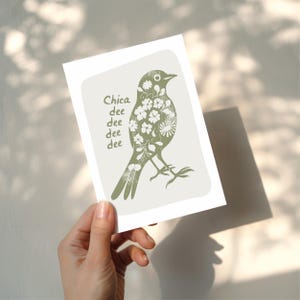 Puede incluir: Tarjeta de felicitaci&oacute;n con una ilustraci&oacute;n de p&aacute;jaro verde llena de patrones florales. Las palabras "Chica dee dee dee dee" est&aacute;n impresas a la izquierda. La tarjeta se sostiene sobre un fondo claro, con sombras proyectadas.