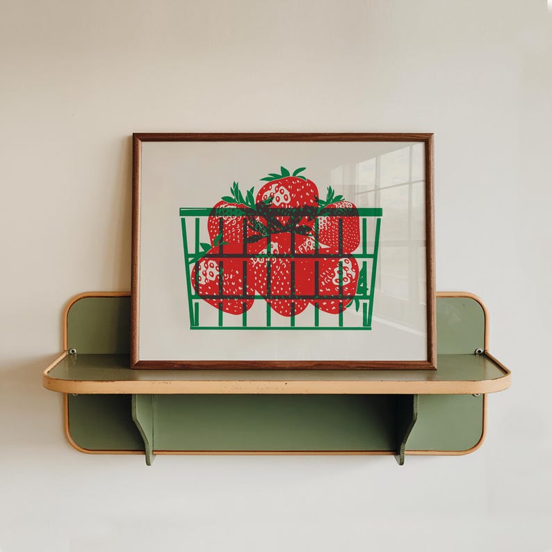 K&ouml;nnte beinhalten: Ein gerahmter Druck eines gr&uuml;nen Drahtkorbs gef&uuml;llt mit roten Erdbeeren. Der Druck h&auml;ngt an einem gr&uuml;nen Regal mit einer hellbraunen Oberseite.