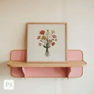 May include: A wooden framed print of a bouquet of flowers in shades of orange, yellow, and pink. The print rests on a two-tiered shelf with a light wood top and pink accents. The shelf is mounted on a cream-colored wall.