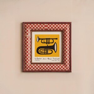 May include: A framed print of a black and white illustration of a trumpet and a trombone on a yellow background. The text "Schooner Jazz Music Festival" is printed below the instruments.