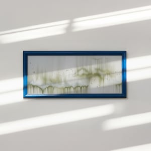 May include: A rectangular artwork with a deep blue frame. The artwork features a white background with abstract green and white paint strokes, creating a blurred, dripped effect. The piece is mounted on a white wall, with sunlight casting shadows.