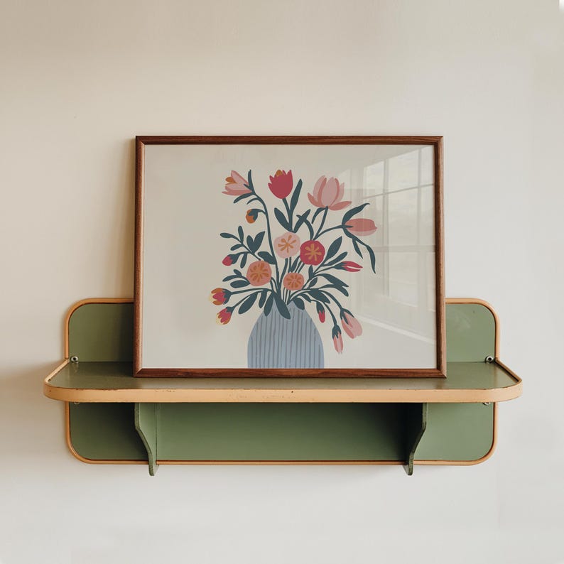 K&ouml;nnte beinhalten: Ein gerahmter Druck eines bunten Blumenarrangements in einer blau-wei&szlig; gestreiften Vase. Der Druck wird auf einem gr&uuml;nen Regal mit einer hellbraunen Verkleidung gezeigt.