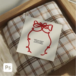 May include: A folded plaid blanket in shades of white, brown, and tan, resting in a wooden tray. A white card with a red line drawing of a bow and the text "Hope your season is merry, bright, and full of delight" is on top.