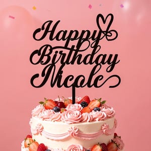 Può includere: Una torta a due piani decorata con vortici di glassa rosa, fragole fresche, lamponi e mirtilli. Un topper per torta nero con il testo Happy Birthday Nicole e un simbolo a forma di cuore è inserito nella parte superiore della torta.