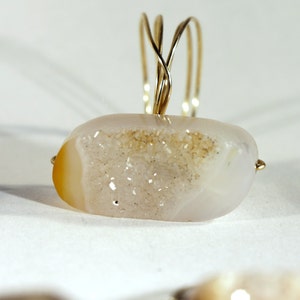 May include: A ring featuring a white agate stone with a brown druzy center, set in a gold wire band.