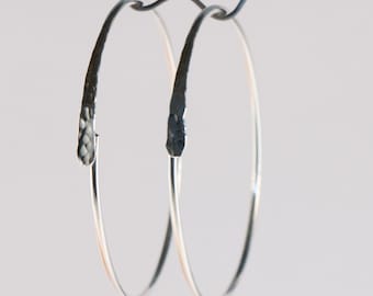 May include: A pair of silver hoop earrings with a hammered texture. The hoops are simple and elegant.