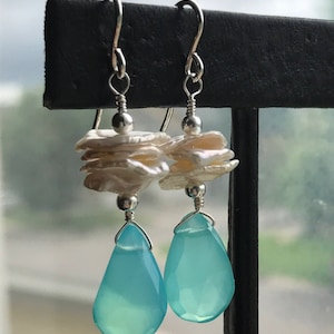 Puede incluir: Pendientes de plata con una piedra preciosa azul en forma de lágrima y un racimo de perlas blancas.