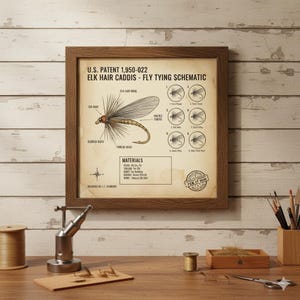 May include: A framed print of a fly tying schematic, featuring an Elk Hair Caddis fly design. The print includes diagrams and material details, with text reading "U.S. Patent 1,950-022." The wooden frame sits on a wooden desk with fly tying tools.