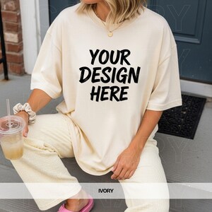 May include: Ivory-colored oversized t-shirt with the text "YOUR DESIGN HERE" in black. The shirt is paired with matching ivory pants. The word "IVORY" is printed at the bottom of the image. The model is wearing a gold necklace and a scrunchie.